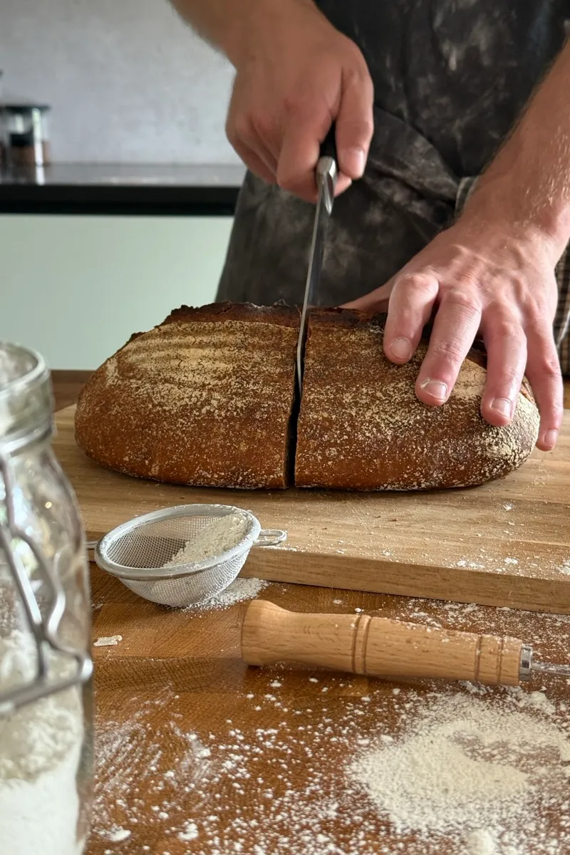 Handen snijden een vers brood open op een houten plank, met mes en meel.
