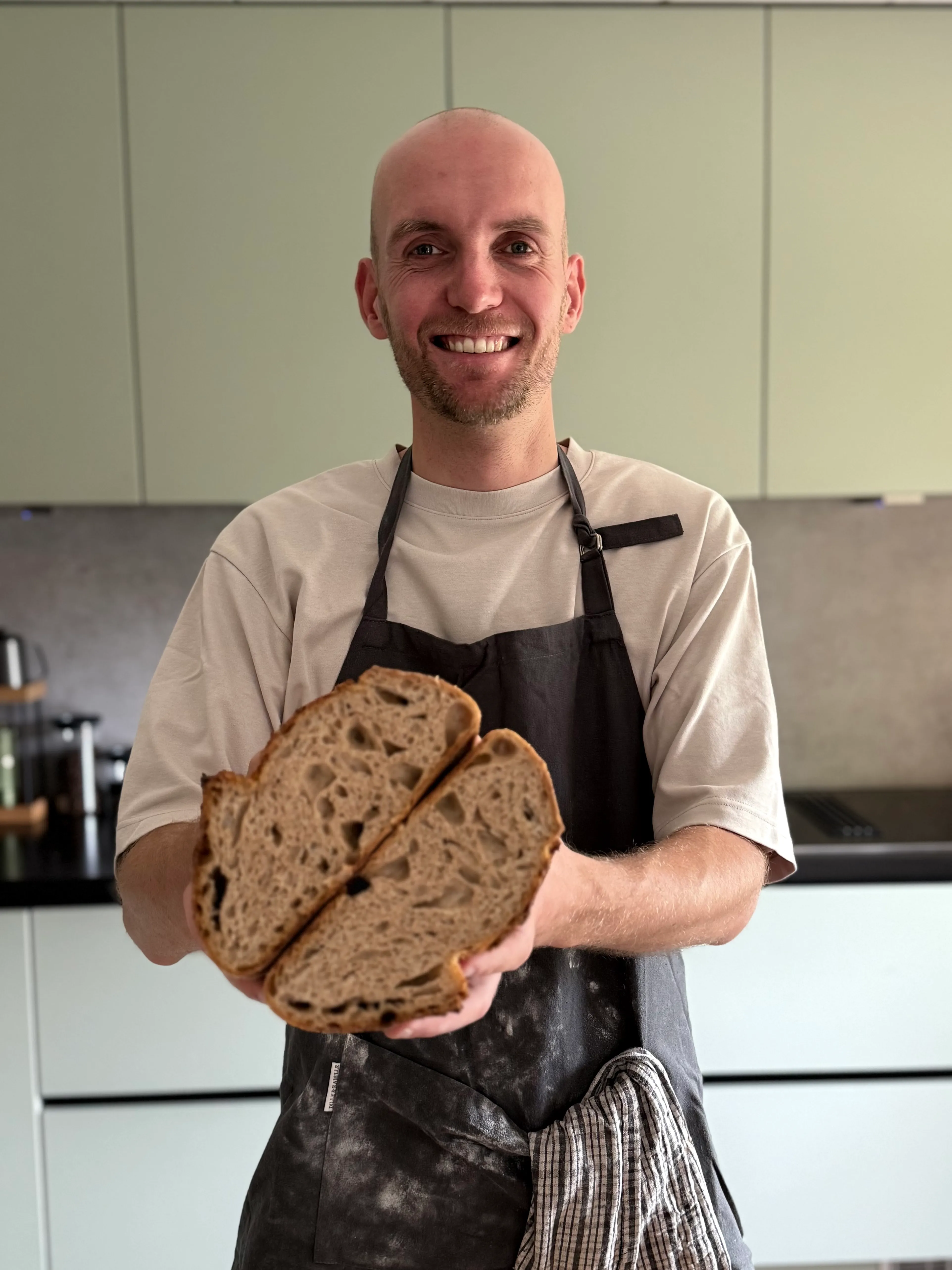 Richard lacht naar de camera met een doorgesneden zuurdesembrood, open kruim zichtbaar.